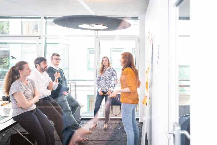 A team stands in front of a planning wall while one person explains something