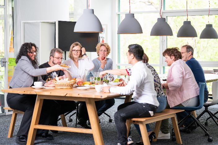 Eight employees have breakfast together at a long wooden table